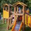 Alpha playhouse with slide su un parco giochi erboso con bambini che giocano.