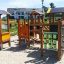 Alpha playhouse with slide in un parco giochi soleggiato, circondato da sabbia ed edifici residenziali in th