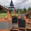 Campanille playground castle in legno con scivoli e strutture per arrampicata in un parco.
