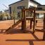 Casetta da gioco in legno 'Spillikins' con scivolo e struttura da arrampicata in un parco giochi.