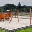 Double Safety Seat double swing su un parco giochi sabbioso con scivolo e strutture per arrampicata.