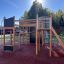 Casetta da gioco in legno Climbing Booth Nature con scivolo e elementi da arrampicata in un parco giochi.