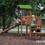 Triangle Modern Nature wooden playhouse with slide in un contesto di parco