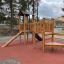 Triangle Modern Nature wooden playhouse with slide in un parco giochi.