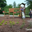Triangle Modern Nature wooden playhouse with slide in un ambiente di parco con bambini che giocano.