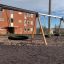Triple swing con sedili di pneumatici nell'area giochi davanti a un edificio in mattoni.
