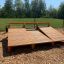 Panca per sit-up realizzata con assi di legno, posizionata all'aperto su una superficie di trucioli di legno, con vegetazione e alberi