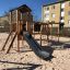 Area giochi in legno Romping Cottage con scivolo ed elementi per arrampicarsi.