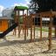 Attrezzatura da gioco all'aperto Romping Cottage con scivolo, reti da arrampicata e casetta in legno.