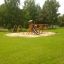 Set da gioco in legno Romping Cottage con scivolo e altalene in un parco verde