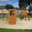 Set da gioco in legno Romping Cottage con reti da arrampicata e scivoli in un parco.