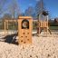 Struttura da gioco in legno Romping Cottage con parete da arrampicata e pavimentazione in sabbia.