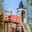 Alcazar playground castle con scivolo e struttura da arrampicata in un parco.