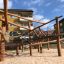 Casetta da gioco in legno Sonora su un parco giochi sabbioso con corde da arrampicata e travi in legno.