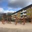 Casetta da gioco in legno Sonora in un parco giochi con edifici residenziali sullo sfondo.
