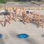 Struttura da arrampicata in legno Sonora con tre trampolini interrati blu in un parco giochi sabbioso