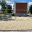 Swing Metal Frame 2+2 (multiple swing) su un parco giochi sabbioso con alberi ed edifici sullo sfondo