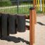 Struttura da gioco Drums con pali in legno e tamburi cilindrici neri su una superficie sabbiosa.