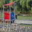 Neptune single playhouse con tetto rosso e pannello blu in un parco giochi.