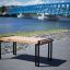 Thor table con gambe in metallo nero e piano in legno posizionato vicino al fiume.