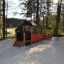 Locomotive with cars train playhouse in un parco giochi sabbioso circondato da alberi.