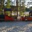 Parco giochi Locomotive with cars train playhouse in un'area sabbiosa circondata da alberi.