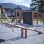 Nature Seesaw in legno in un moderno parco giochi con strutture da arrampicata sullo sfondo.