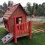 Casetta da gioco in legno con dettagli rossi ed elementi di arrampicata da Anna's Playhouse.