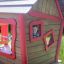 Casetta da gioco in legno con finiture rosse e un bambino sorridente che sbircia dalla finestra da Anna's Playhouse