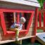 Bambino che gioca in Anna's Playhouse set da gioco in legno con dettagli rossi.