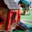 Casetta da gioco in legno per bambini con accenti rossi della linea Anna's Playhouse in un parco giochi.