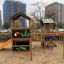 Jungle House playhouse with slide in un parco giochi con edifici cittadini sullo sfondo.