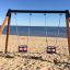 Double Baby Swing posizionato su una spiaggia sabbiosa con vista sul mare.