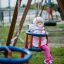 Double Baby Swing con un bambino in un outfit rosa che si diverte sull'altalena in un parco giochi.