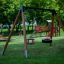 Un Double Swing in legno posizionato su un parco giochi verde.