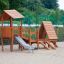 Galapagos wooden playhouse with slide in un'area giochi sabbiosa.