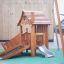Tambora wooden playhouse with slide su un'area giochi con parete da arrampicata e pavimentazione di sicurezza verde
