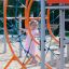 Bambino che si arrampica sulla struttura da gioco Ursa Maior arancione e blu con scivolo e rete da arrampicata