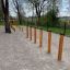 Agility Weave Poles allestito all'aperto su una superficie di ghiaia con alberi sullo sfondo.