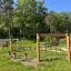 Struttura in legno per esterni 'Obstacle course' in un parco verde con reti da arrampicata e travi di equilibrio.