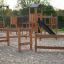 Attrezzatura da gioco in legno Trim trail con strutture da arrampicata e scivolo su terreno sabbioso.