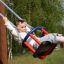 Bambino che gioca su Wooden Baby double swing con sedile rosso e blu in un parco.