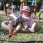 Due bambini seduti su un Bird Nest Single Swing (BNS 120 cm) che leggono un libro in un parco giochi.
