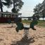 Gioco a molla Green Rabbit Rocking per parco giochi su terreno sabbioso con alberi e lago sullo sfondo
