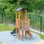 Pixie Modern Nature wooden playhouse with slide nel parco giochi con scala da arrampicata e rete di sicurezza