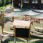 Aula all'aperto con panche in legno, tende parasole, lavagna e vasi per piante in un contesto di parco giochi
