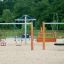 Nature Double Swing su un parco giochi sabbioso con alberi sullo sfondo.