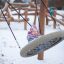 Bambino che gioca sulla Single Swing in un parco giochi innevato.