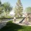 Bambini che giocano sul set da gioco Alstad Eco in un parco con alberi verdi e prato.