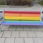 Colourful bench con doghe in legno color arcobaleno e struttura in metallo in un'area esterna pavimentata.